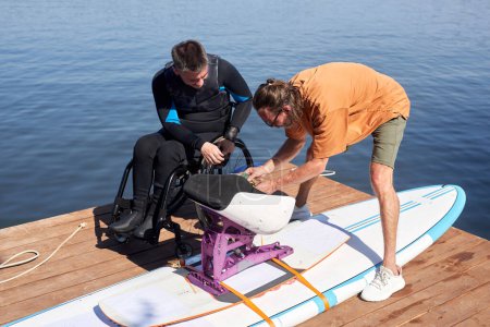 Blick aus der Vogelperspektive auf Sportlehrer, der Menschen mit Behinderung hilft und adaptive Wakeboarding-Ausrüstung montiert