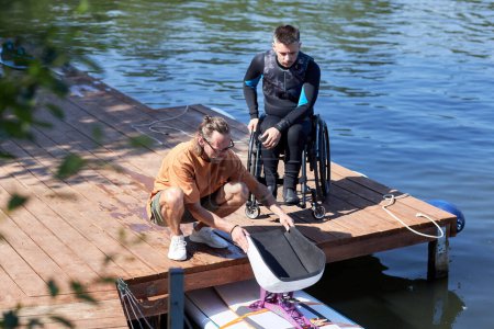 Téléchargez les photos : Portrait d'un moniteur de sports nautiques préparant du matériel de wakeboard adaptatif pour homme handicapé à l'extérieur - en image libre de droit
