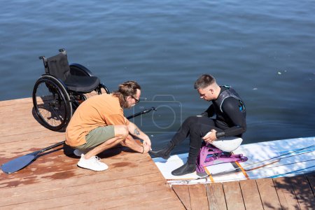 Seitenansicht Porträt eines Ausbilders, der Mann mit Behinderung beim Wakeboarden mit adaptiver Ausrüstung unterstützt