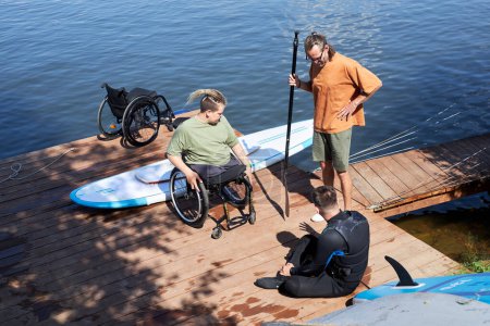 Hochwinkelporträt eines erfahrenen Sportlehrers, der Menschen mit Behinderungen am Pier Vorführungen über Wassersport und adaptive Ausrüstung gibt