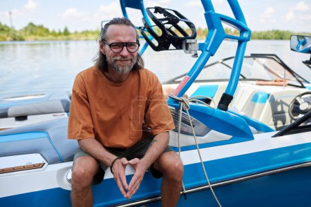 Portrait of smiling bearded man sitting on boat enjoying water sports outdoors, copy space