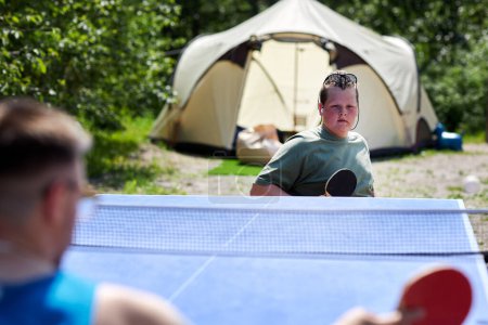 Téléchargez les photos : Portrait de jeune homme handicapé jouant au tennis de table avec un partenaire à l'extérieur pendant le voyage de camping - en image libre de droit