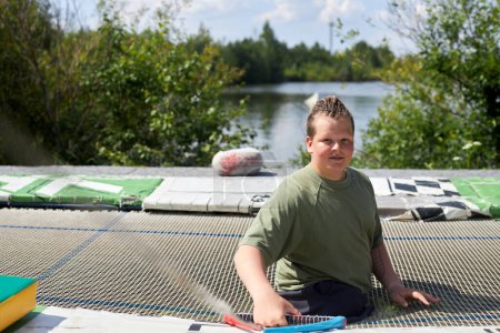 Téléchargez les photos : Full length portrait of smiling young man with disability looking at camera outdoors in water sports club, copy space - en image libre de droit