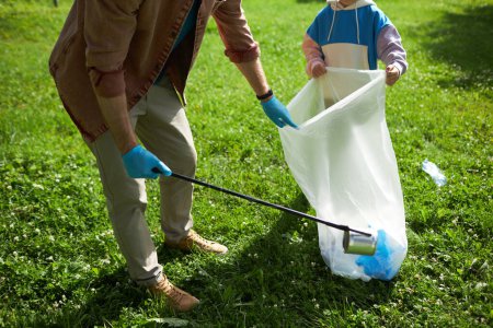 Photo for High angle closeup of father and son picking up trash outdoors helping clean nature in sunlight, copy space - Royalty Free Image