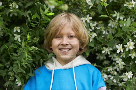 Photo for Front view portrait of smiling blonde boy in flowering bush outdoors looking at camera - Royalty Free Image