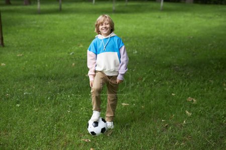 Téléchargez les photos : Portrait pleine longueur de sourire entre garçon avec ballon de football à l'extérieur debout sur l'herbe verte, espace de copie - en image libre de droit