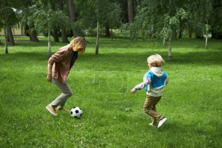 Téléchargez les photos : Plan d'action complet du père et du fils jouant au football ensemble sur l'herbe verte dans le parc, espace de copie - en image libre de droit