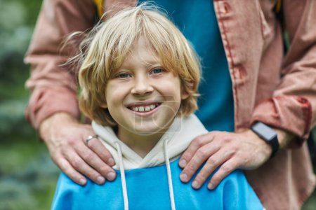 Photo for Closeup of smiling blonde boy looking at camera with fathers hands on shoulders - Royalty Free Image
