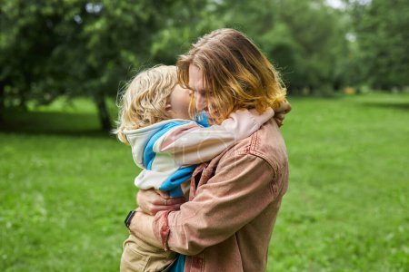 Photo for Side view portrait of happy father embracing blonde little boy in park carefree, copy space - Royalty Free Image