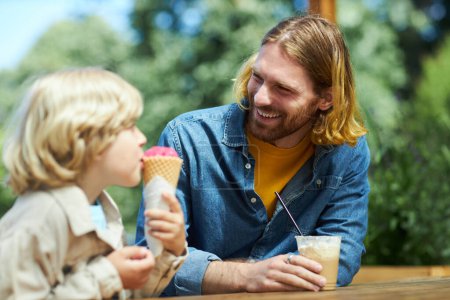 Foto de Retrato de feliz padre e hijo en el parque de atracciones comiendo helado al aire libre juntos - Imagen libre de derechos
