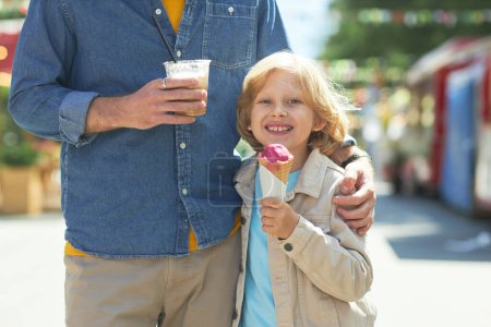 Photo for Portrait of happy father and son in amusement park eating ice cream and enjoying bonding time together - Royalty Free Image