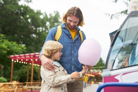Photo for Side view portrait of happy father and son buying cotton candy at festival - Royalty Free Image