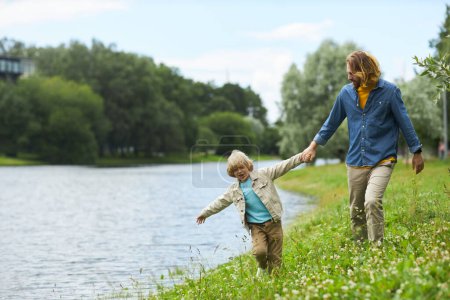 Téléchargez les photos : Portrait complet du père et du fils marchant ensemble au bord du lac dans la forêt verte, espace de copie - en image libre de droit