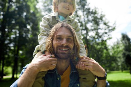 Photo for Closeup portrait of happy young father carrying son on shoulders outdoors in sunlight - Royalty Free Image