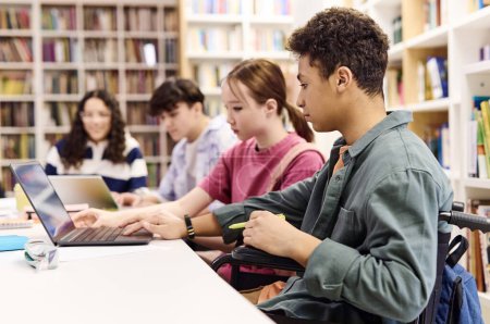 Foto de Retrato de vista lateral de grupo multiétnico de estudiantes que usan computadora portátil en la biblioteca sentados en la mesa en el espacio de copia de fila - Imagen libre de derechos