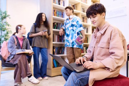Photo for Side view portrait of smiling teenage boy using laptop in school library lounge with group of students copy space - Royalty Free Image