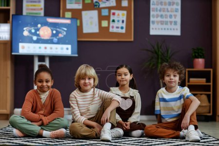 Photo for Front view of diverse group of little kids sitting on floor in preschool class and looking at camera, copy space - Royalty Free Image
