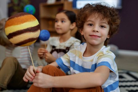 Foto de Retrato de un lindo niño sosteniendo el modelo del planeta y sonriendo a la cámara en la clase preescolar - Imagen libre de derechos
