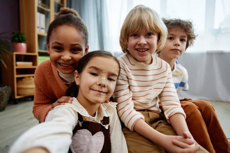 Foto de Diverso grupo de niños pequeños tomando foto selfie y sonriendo a la cámara en la clase preescolar o jardín de infantes - Imagen libre de derechos