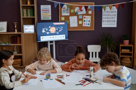 Foto de Diverso grupo de niños pequeños haciendo artes y manualidades sentados en la mesa en la clase preescolar, espacio para copiar - Imagen libre de derechos