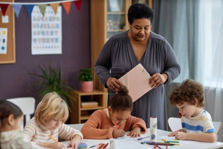 Photo for Portrait of kind Black woman watching little children doing arts and crafts in preschool class, copy space - Royalty Free Image