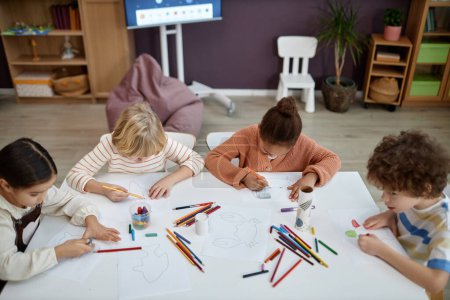 Téléchargez les photos : Vue de dessus d'un groupe multiethnique d'enfants faisant de l'art et de l'artisanat assis à table dans une classe préscolaire, espace pour copier - en image libre de droit