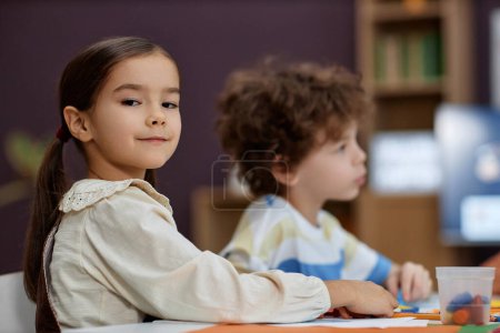 Photo for Portrait of cute smart girl looking at camera while coloring pictures at table in arts and crafts class at preschool, copy space - Royalty Free Image