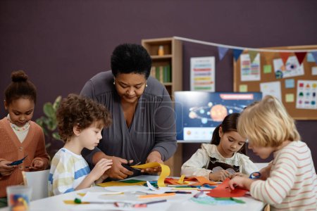 Photo for Portrait of kind Black woman helping group of little children doing crafts in preschool class, copy space - Royalty Free Image