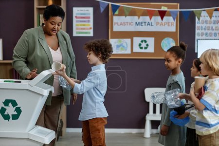 Téléchargez les photos : Portrait latéral de la femme noire enseignant aux petits enfants le recyclage et le tri des déchets à l'école maternelle, espace de copie - en image libre de droit