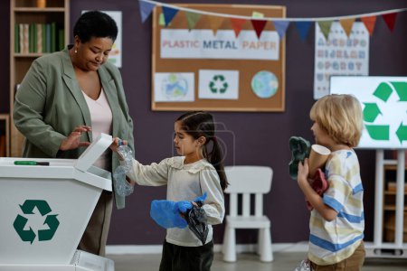 Téléchargez les photos : Portrait latéral de petite fille triant le plastique en classe de recyclage à l'école maternelle, espace de copie - en image libre de droit