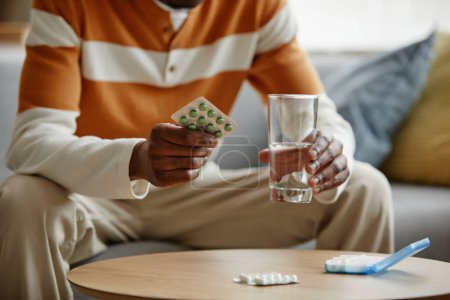 Photo for Close up of Black man holding blister of pills and glass of water while taking medication at home, copy space - Royalty Free Image