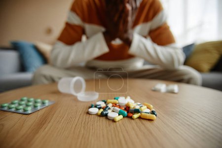 Téléchargez les photos : Gros plan de pile de pilules et de comprimés sur la table avec l'homme noir déprimé en arrière-plan, espace de copie - en image libre de droit