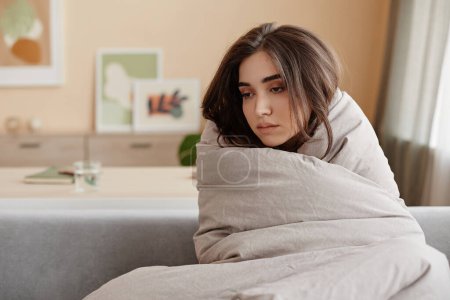 Photo for Portrait of sad young woman wrapped in blankets at home struggling with depression, copy space - Royalty Free Image