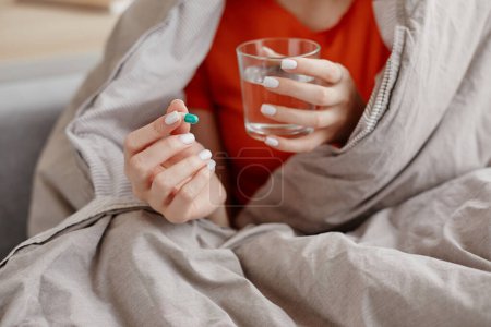 Photo for Closeup of young woman holding pill and glass of water wrapped in blanket, copy space - Royalty Free Image