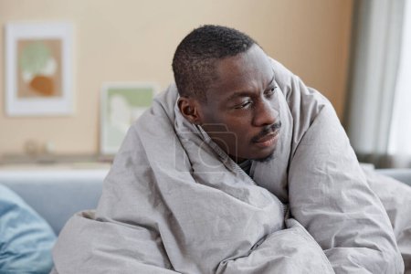 Téléchargez les photos : Portrait d'un homme afro-américain adulte enveloppé dans des couvertures luttant contre la dépression à la maison, espace de copie - en image libre de droit