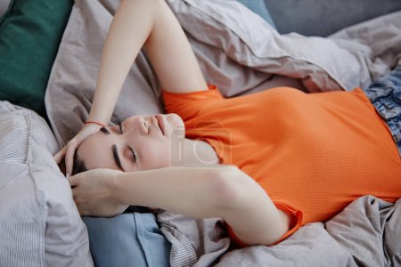 Photo for High angle portrait of sad young woman lying on bed in morning struggling with depression with eyes closed - Royalty Free Image