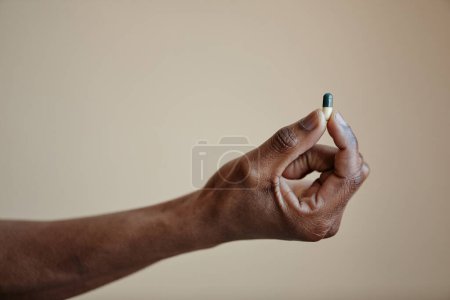 Photo for Closeup of Black male hand holding single capsule pill against neutral background, copy space - Royalty Free Image
