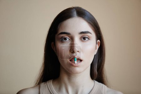 Photo for Closeup portrait of young woman holding single pill in open mouth and looking at camera - Royalty Free Image
