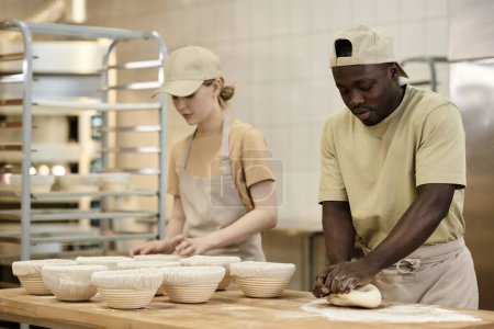 Téléchargez les photos : Portrait taille haute de deux jeunes gens travaillant dans la boulangerie et la pâte à pétrir pour du pain frais, espace de copie - en image libre de droit
