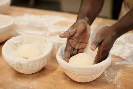 Foto de Primer plano del joven negro cuidadosamente poniendo masa fresca en un tazón en la cocina de la panadería, espacio para copiar - Imagen libre de derechos