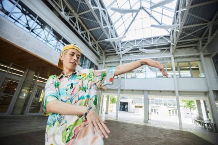 Action-Porträt eines lächelnden jungen asiatischen Mannes, der in einem städtischen Gebäude tanzt, Kopierraum