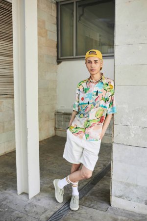 Vertikales Ganzkörperporträt eines jungen Asiaten, der in urbaner Umgebung in sein farbenfrohes flippiges Outfit blickt