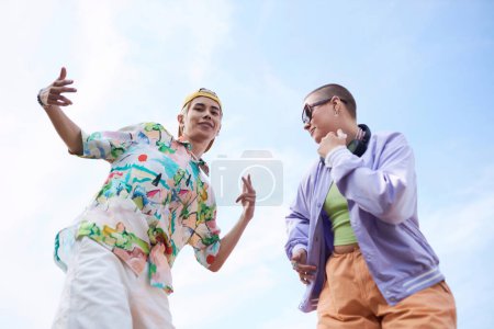 Minimales Porträt zweier flippiger junger Leute, die vor strahlend blauem Himmel tanzen und in die Kamera schauen
