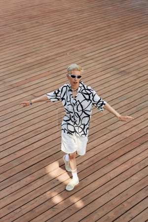 Photo for Vertical wide angle shot of young Asian man dancing hip-hop on wooden deck in city, copy space - Royalty Free Image