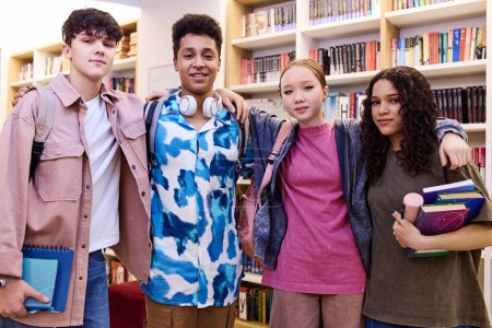 Photo for Waist up portrait of multiethnic group of students standing in school library holding books and smiling at camera - Royalty Free Image