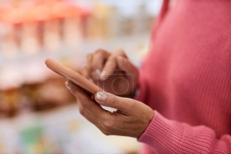 Close up of unrecognizable woman holding smartphone and checking shopping list in supermarket, copy space