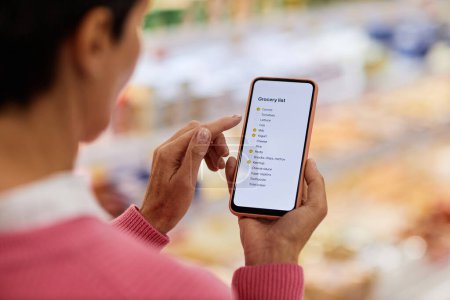 Foto de Primer plano de la mujer adulta leyendo la lista de compras en la pantalla del teléfono inteligente en el supermercado, espacio de copia - Imagen libre de derechos
