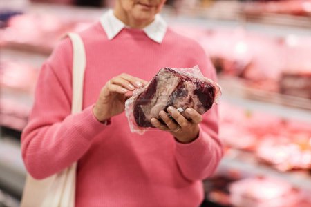 Primer plano de la mujer adulta sosteniendo compras de carne fresca para comestibles en el supermercado, espacio para copias