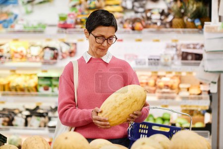 Waist up portrait of adult woman holding big melon while shopping for groceries in supermarket, copy space