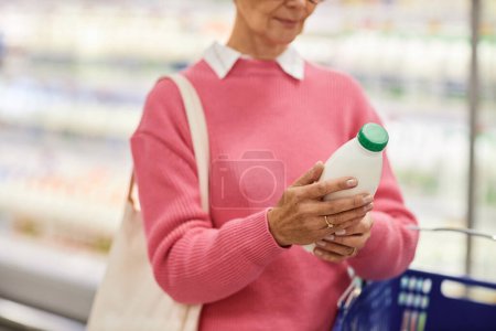 Close up of woman holding bottle of milk in supermarket and looking at expiration dates, copy space